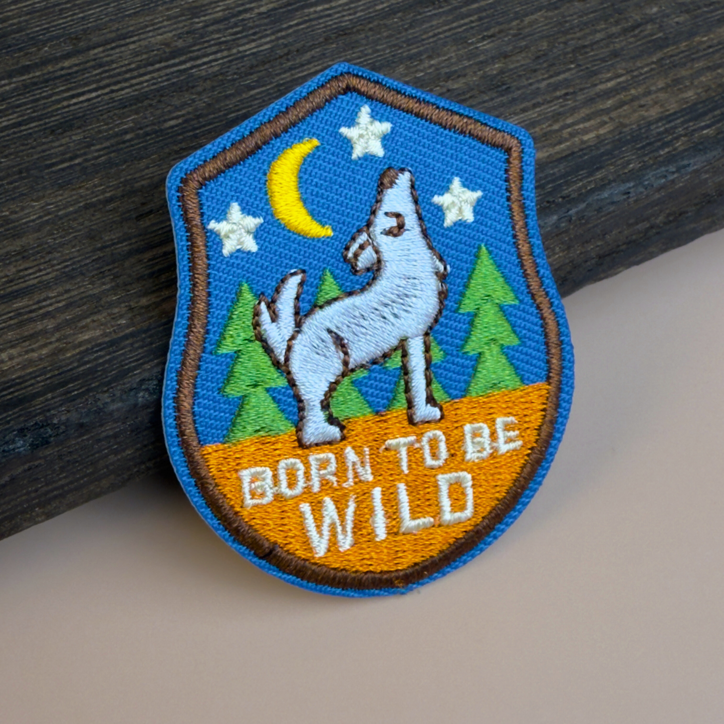 Embroidered patch with a wolf, moon, and stars design that says "Born To Be Wild" on a wooden surface.