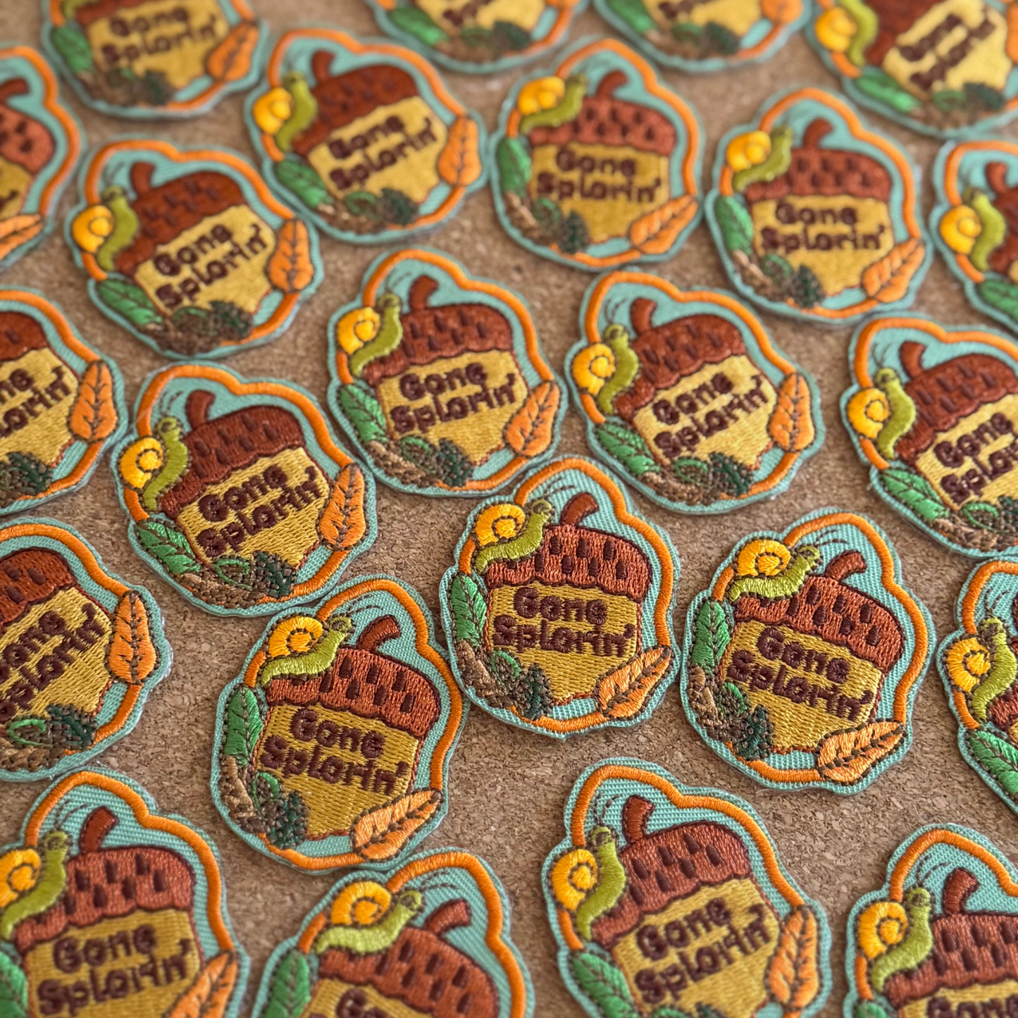 Collection of 'Gone Splorin'' patches with a snail on an acorn and leaves on a brown background.