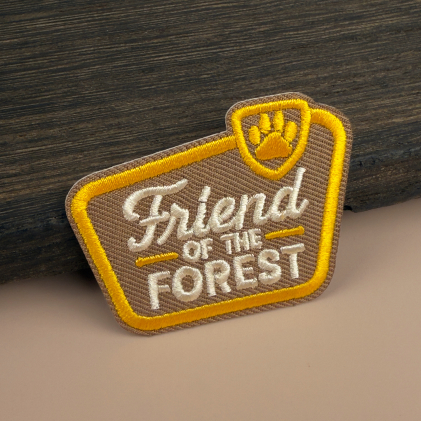 Patch with 'Friend of the Forest' text and paw print in a National Park sign shape, on a wooden background