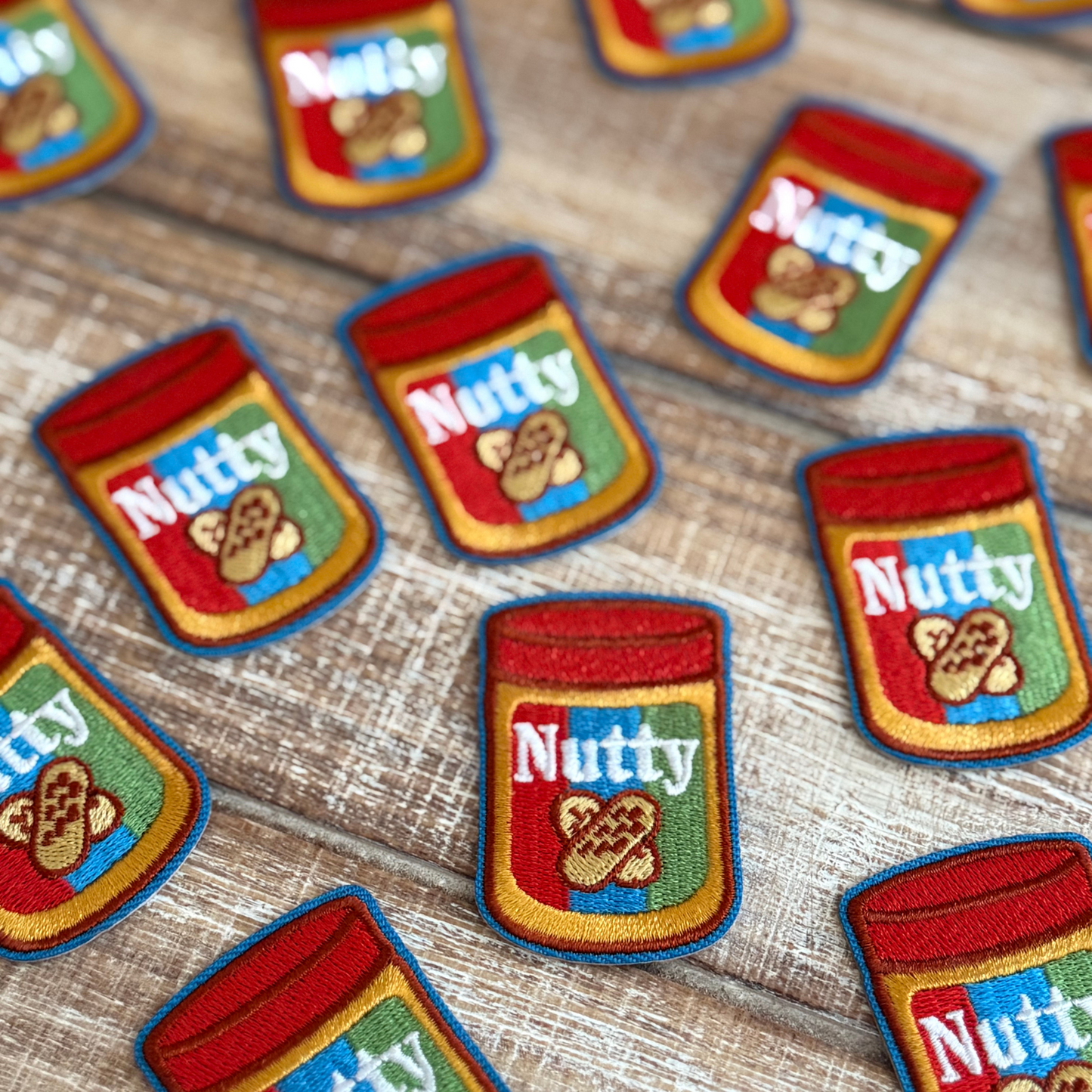 Collection of 'Nutty' peanut butter jar patches on a wooden surface