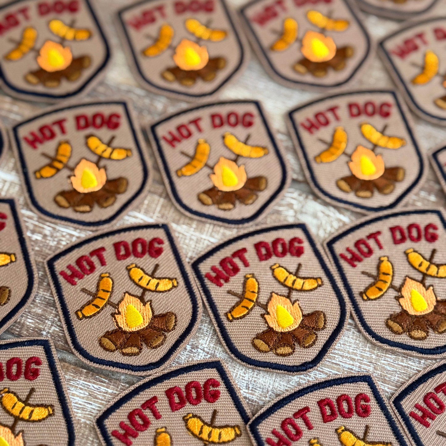 Multiple patches with 'Hot Dog' text and graphic design of hot dogs over a campfire on a textured background