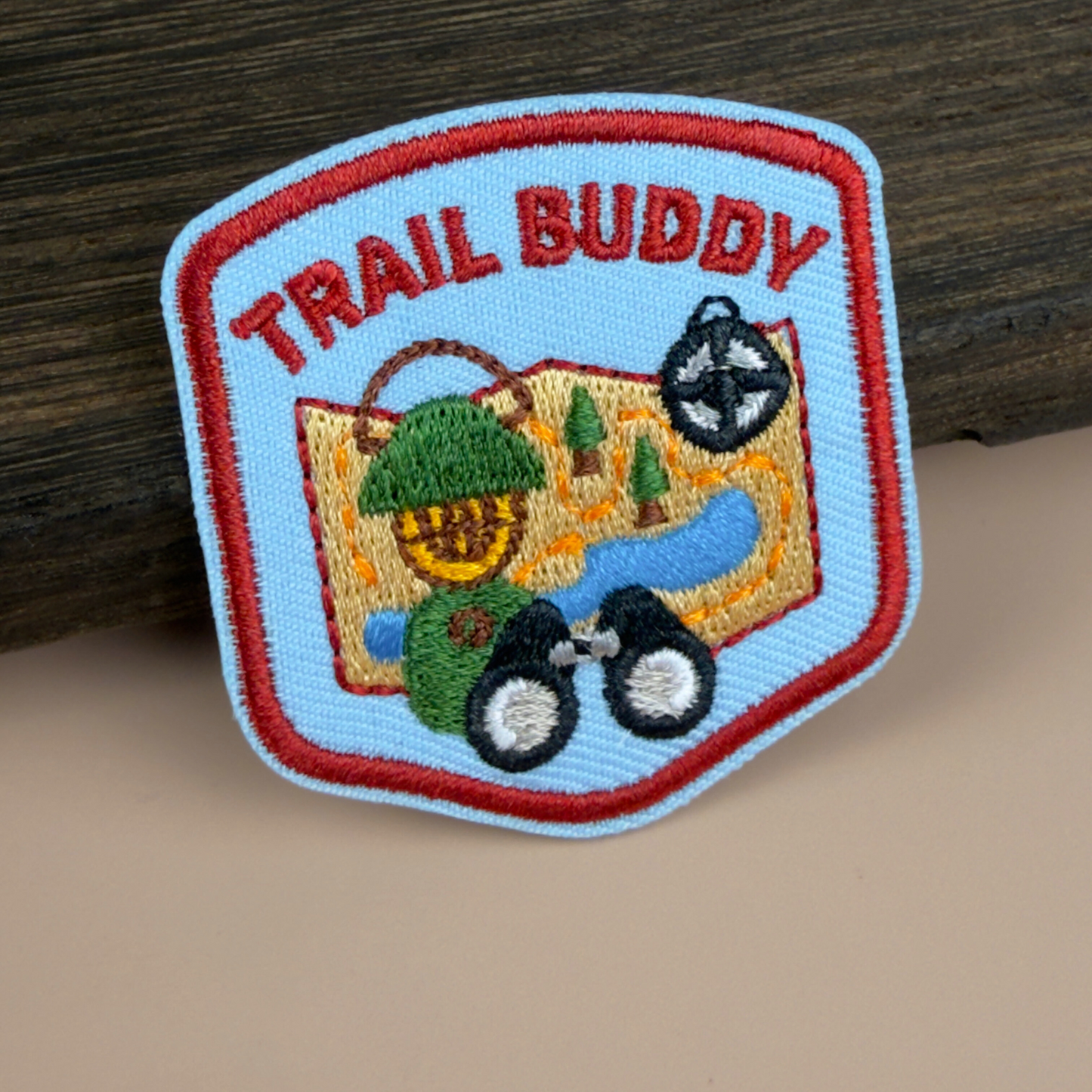 Embroidered patch with 'Trail Buddy' text and outdoor design on a wooden surface