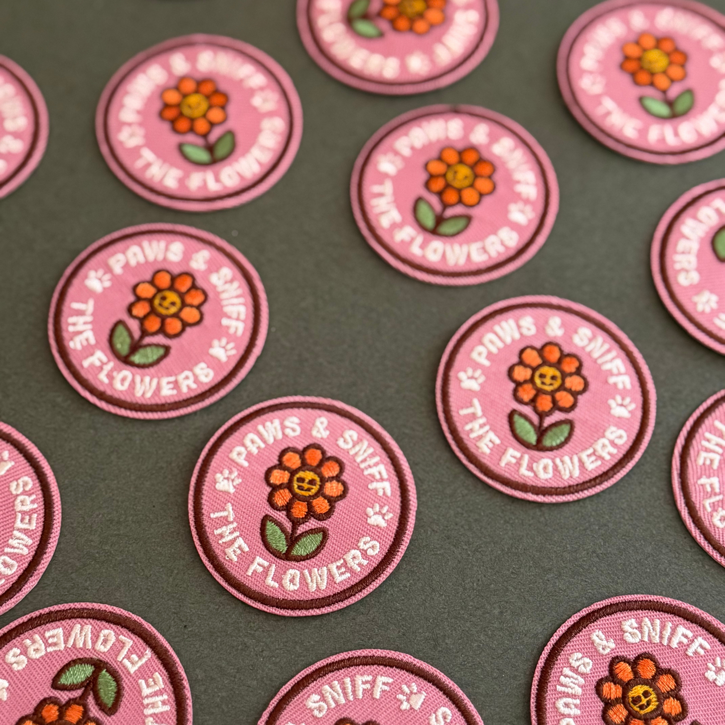 Pink embroidered patches with floral design and "Paws & sniff the flowers" text on a dark green background