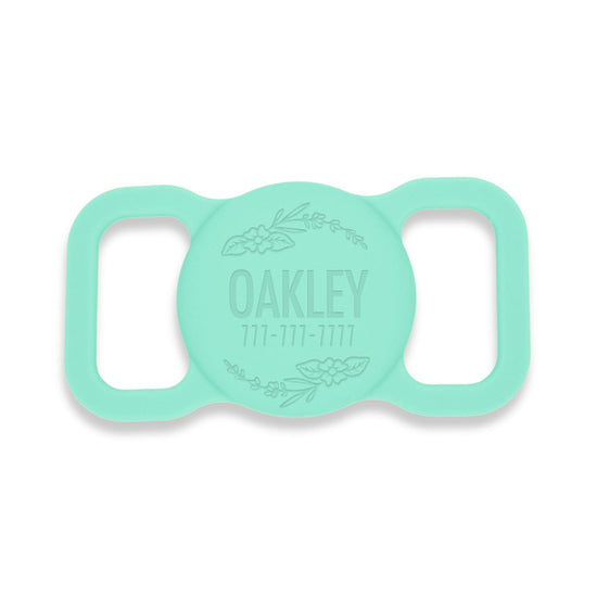 Aqua silicone AirTag holder with a floral design. Pet's name and a phone # is engraved on the front.