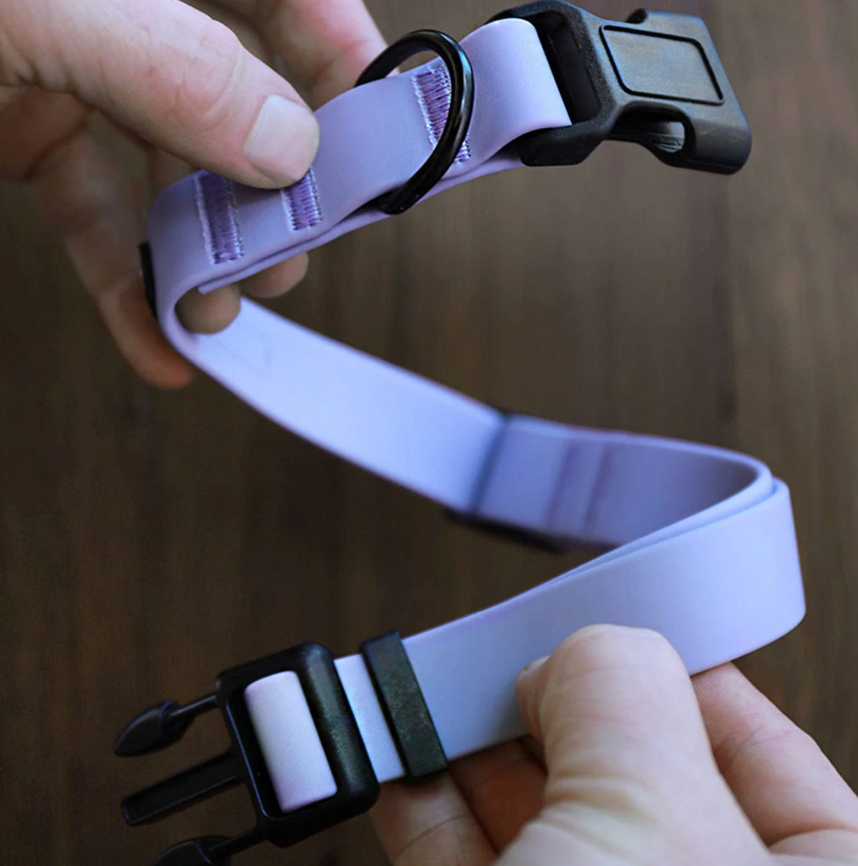 Hands adjusting a purple adjustable dog collar with a black buckle and D-ring, showcasing a secure and durable design for pet comfort and safety.