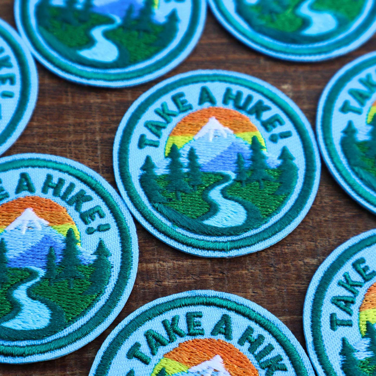 Embroidered patches with 'Take a Hike!' design on a wooden surface