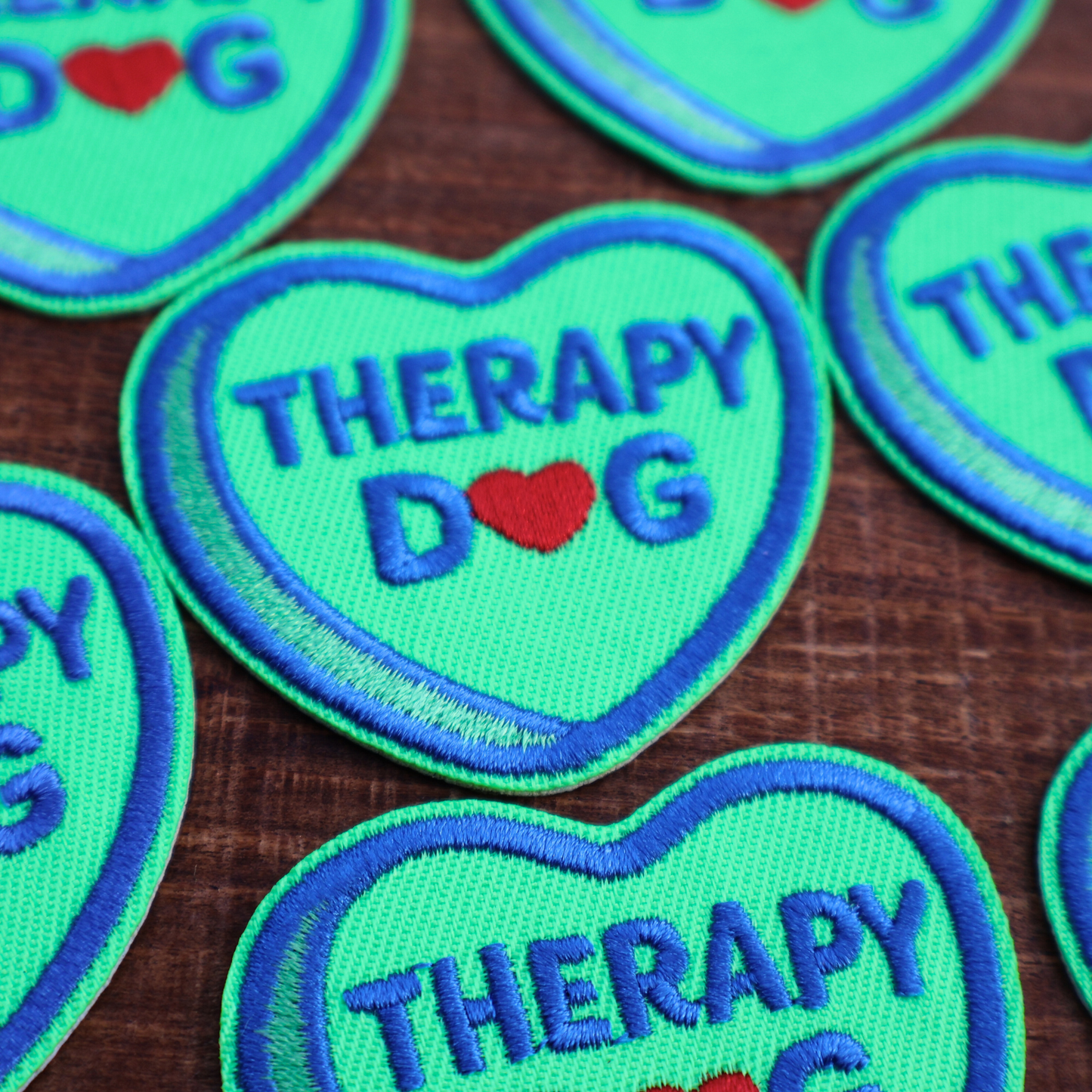 Heart-shaped patches with 'Therapy Dog' text on a wooden surface