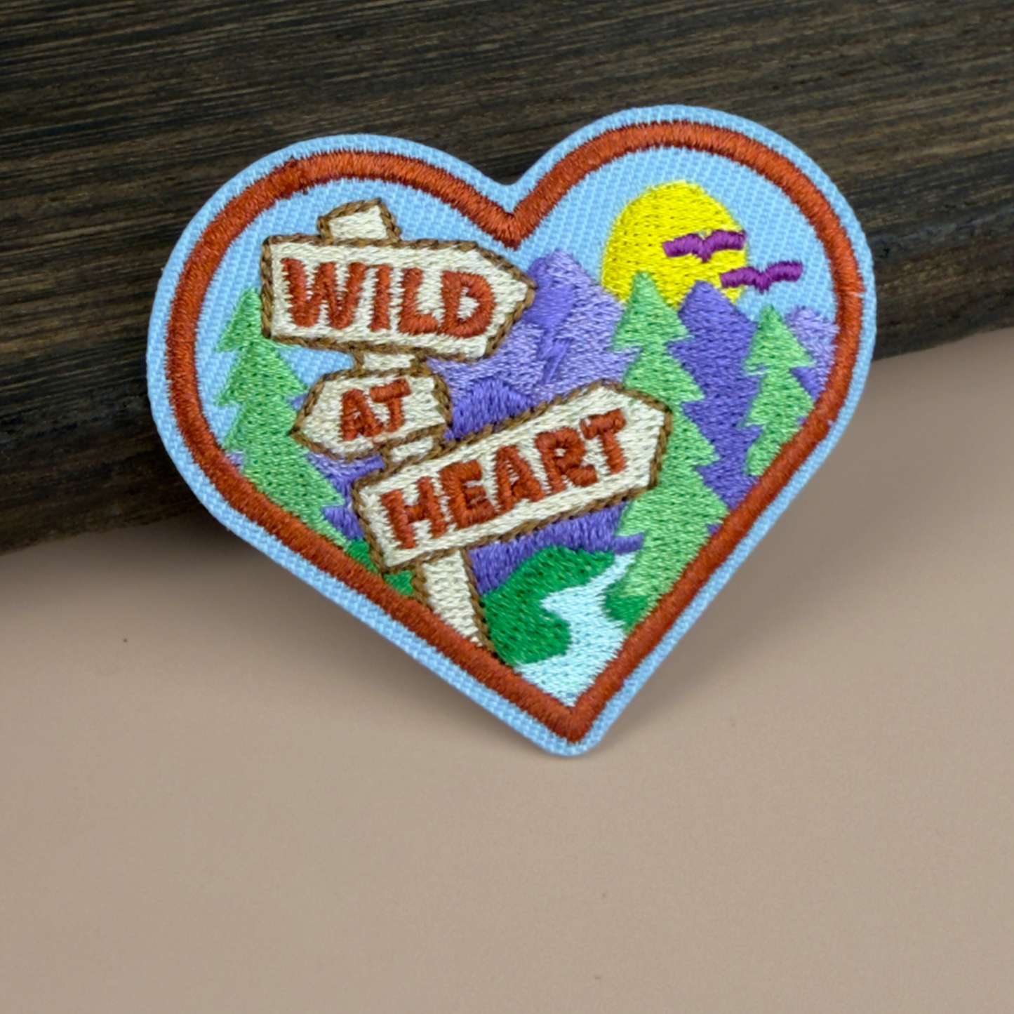 Heart-shaped patch with 'Wild at Heart' text and nature-themed design on a wooden surface
