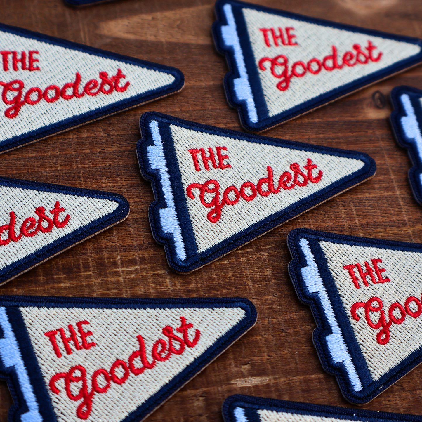 Embroidered patches with 'The Goodest' text on a wooden surface
