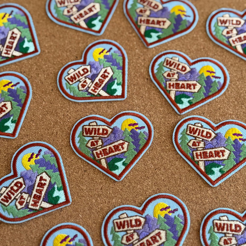 Heart-shaped patches with 'Wild at Heart' text and nature-themed design on a brown background