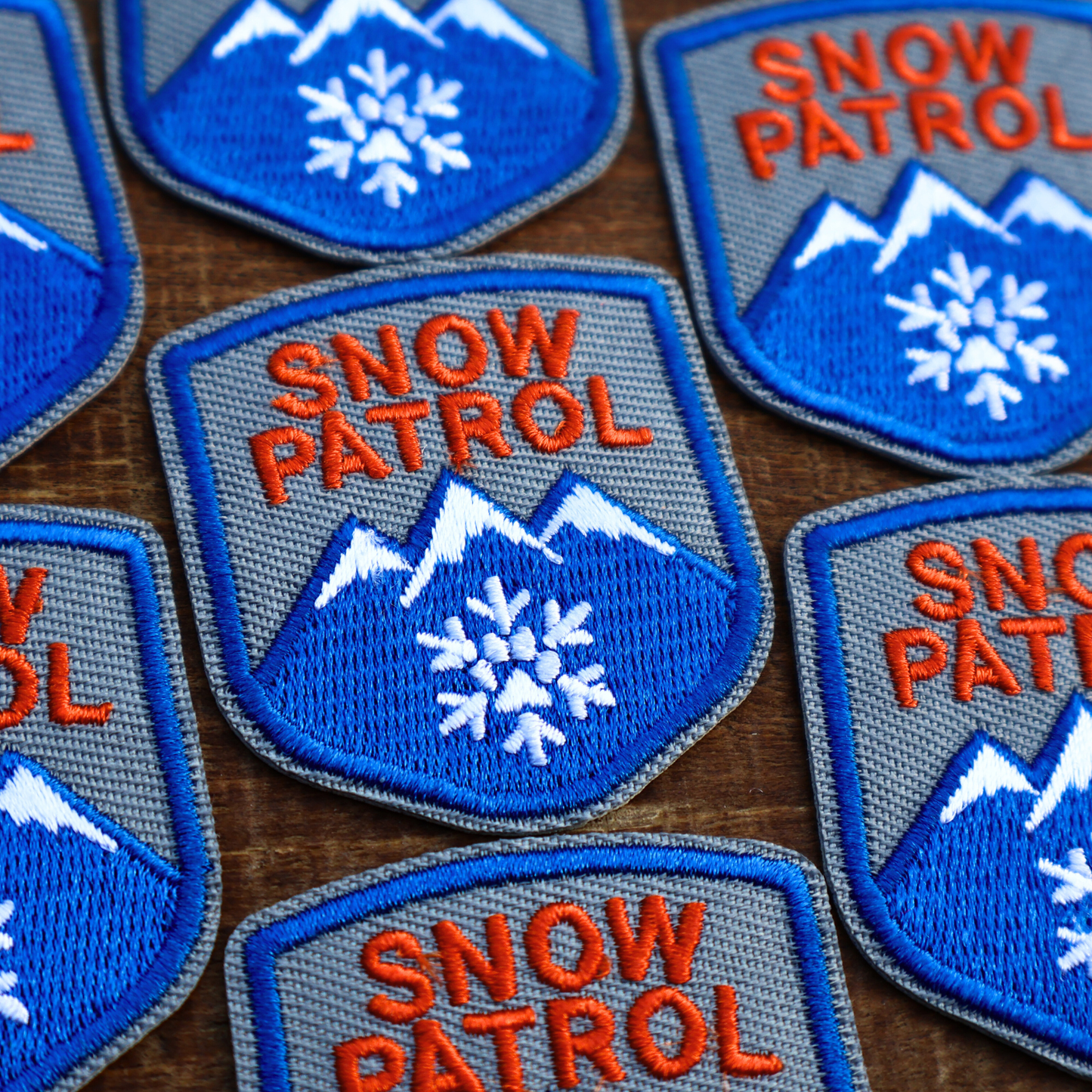 Multiple patches with 'Snow Patrol' text and mountain designs on a wooden surface