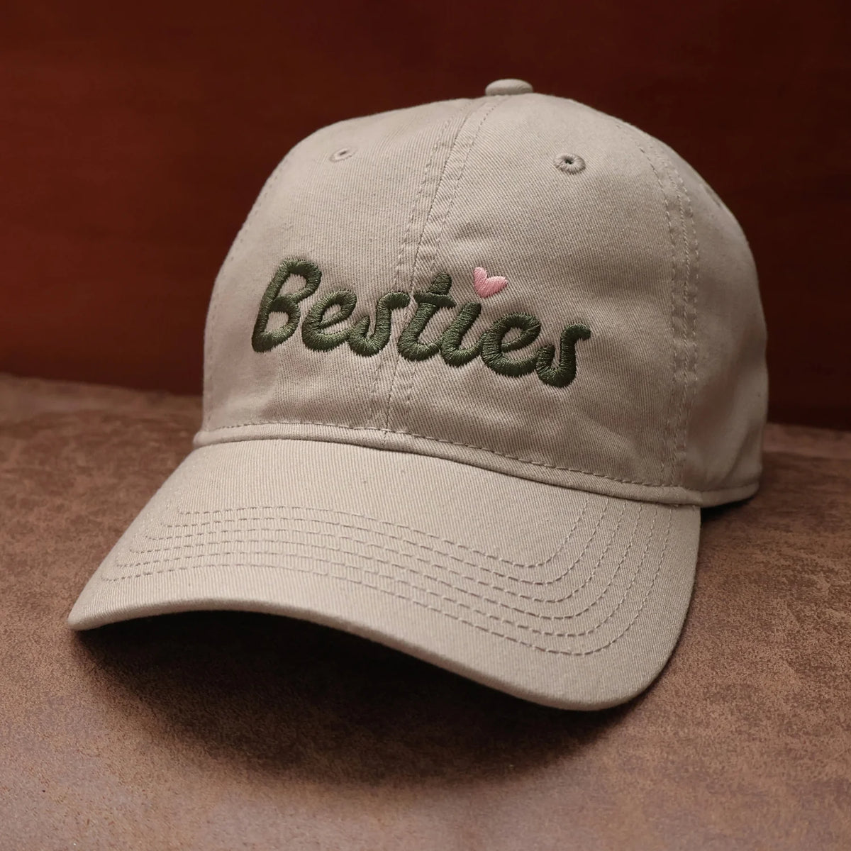 Tan cotton dad hat featuring dark green Besties embroidery and curved brim.