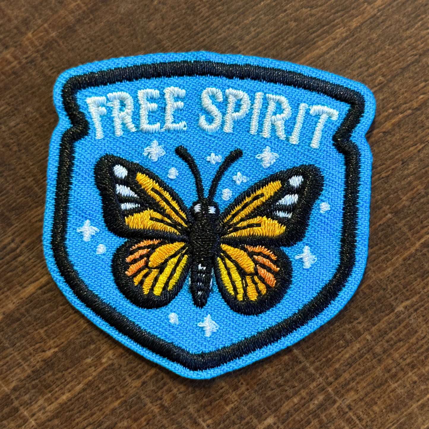 Embroidered iron-on patch with a butterfly and 'Free Spirit' text on a wooden surface