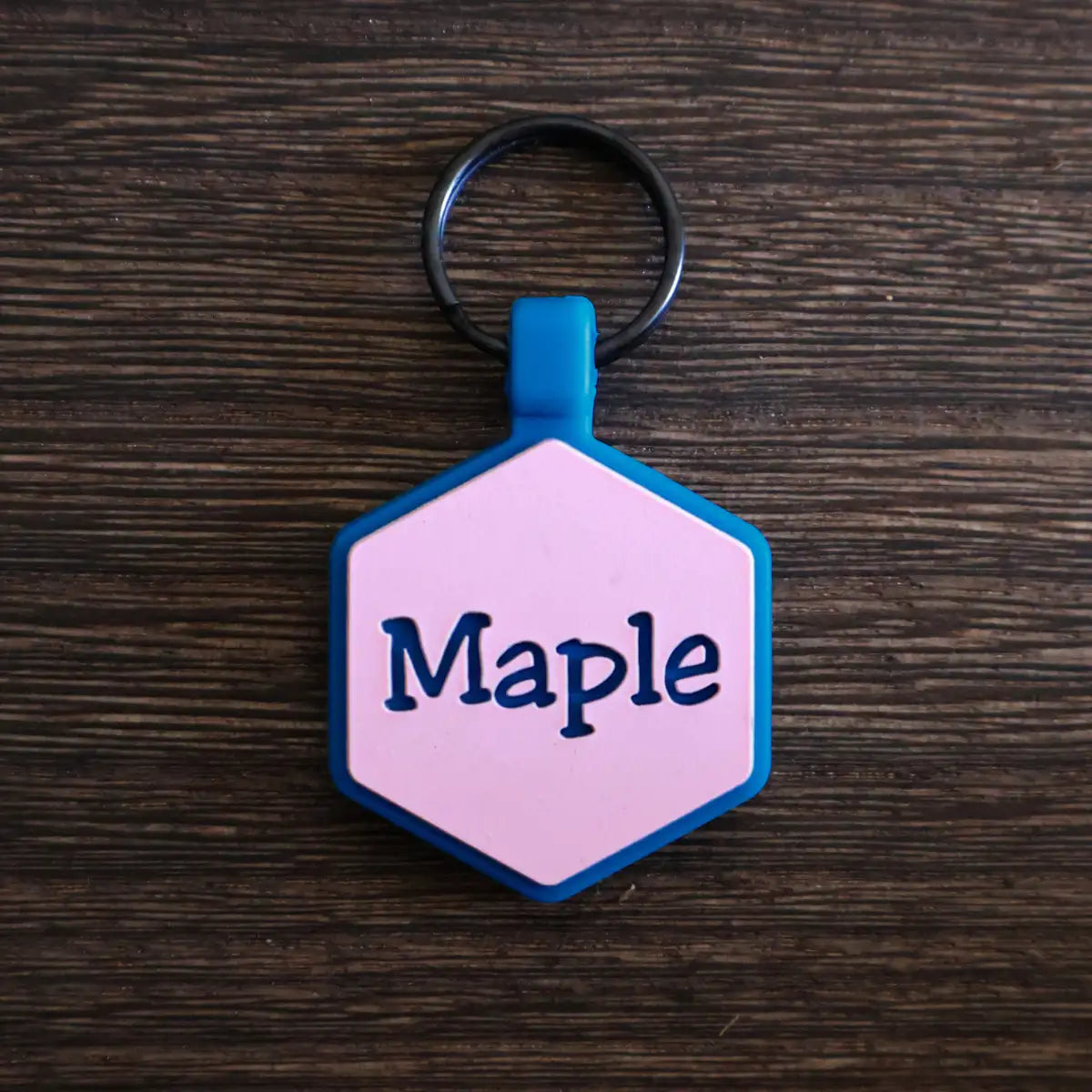 Hexagonal silicone pet ID tag with the name 'Maple' engraved on the front on a wooden surface