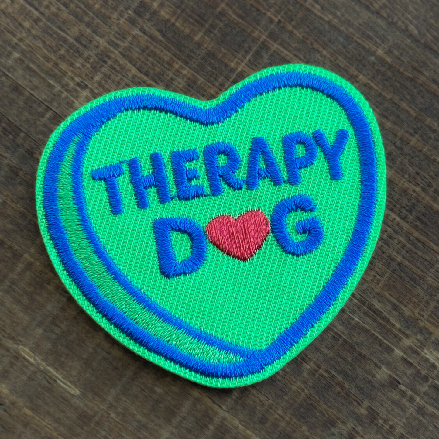 Heart-shaped iron-on patch with 'Therapy Dog' text on a wooden surface
