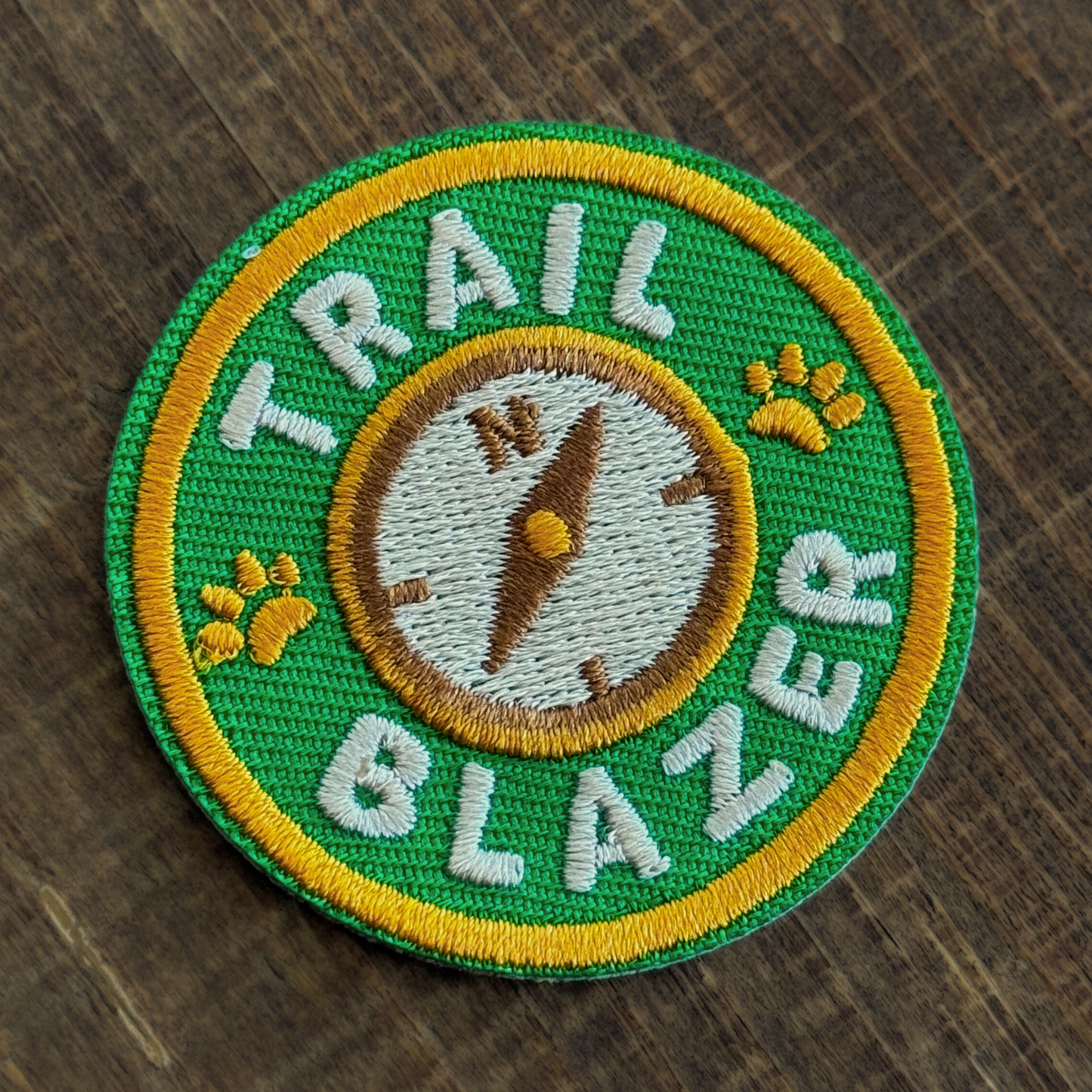 Embroidered iron-on patch with 'Trail Blazer' text and compass design on a wooden surface