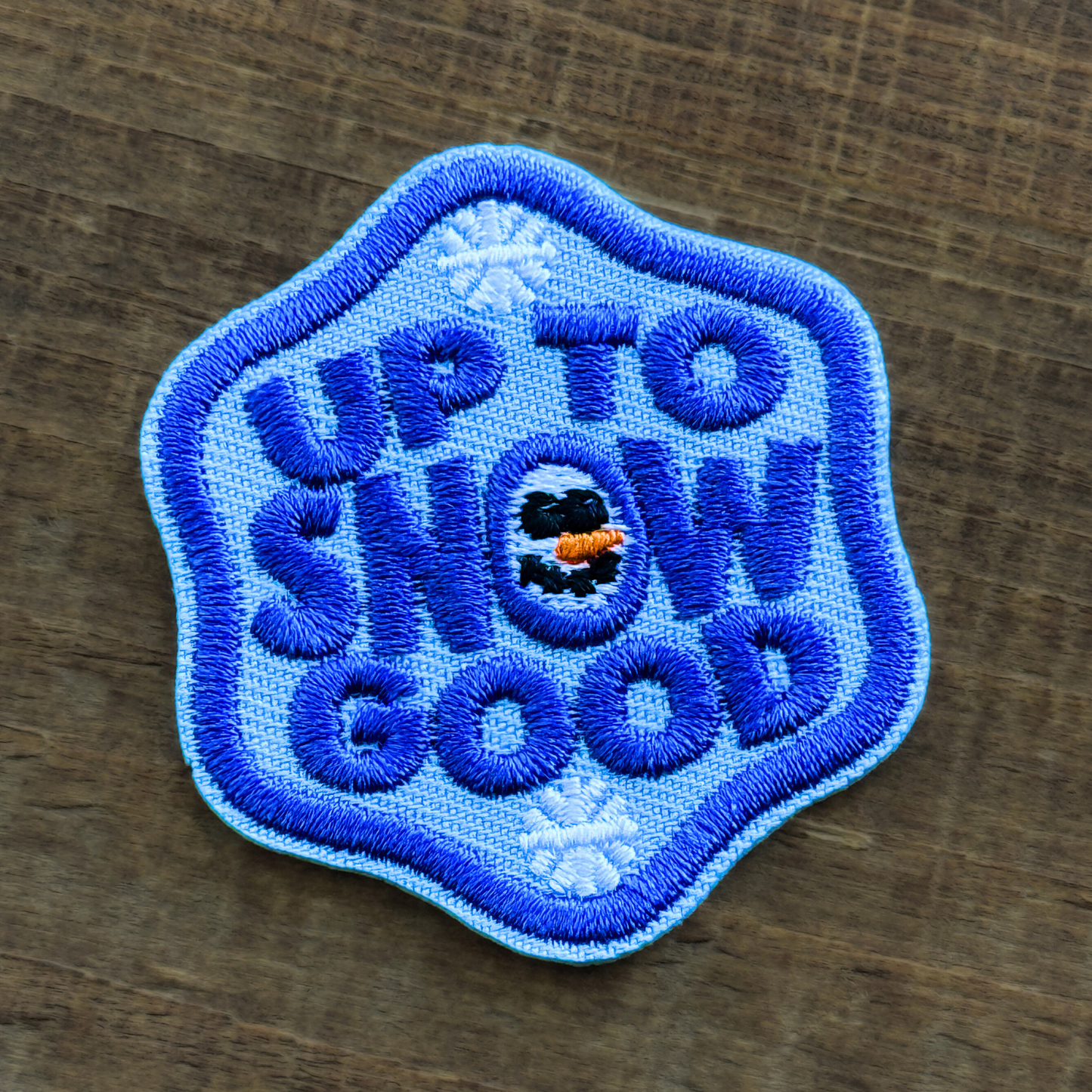 Embroidered patch with 'Up to Snow Good' text on a wooden surface