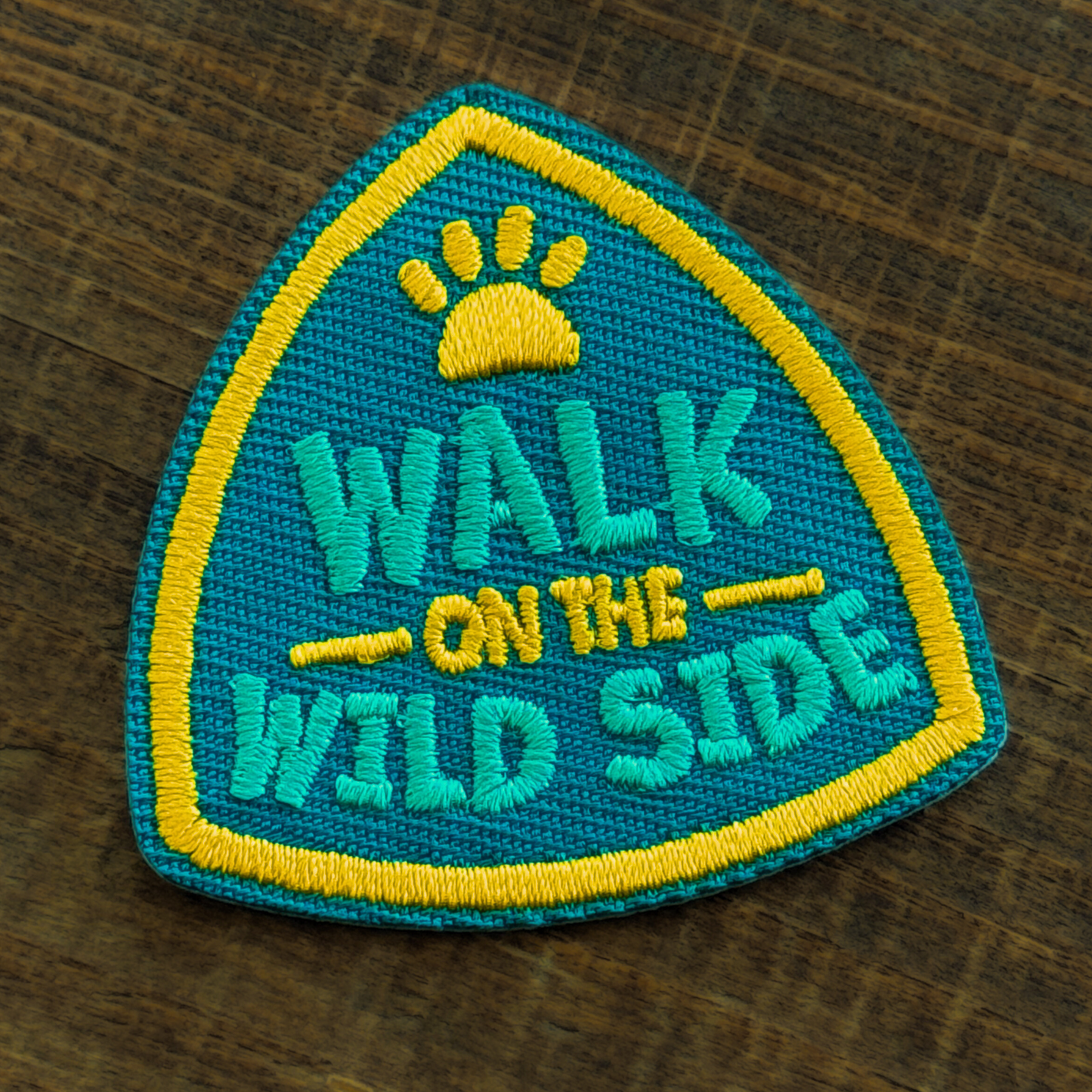 Embroidered iron-on patch for dogs with 'Walk on the Wild Side' text on a wooden surface